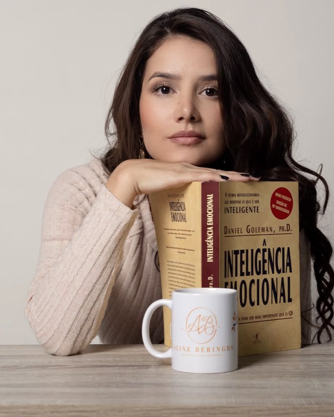 Aline Beringhs à mesa, com o livro Inteligência Emocional e uma caneca com seu monograma