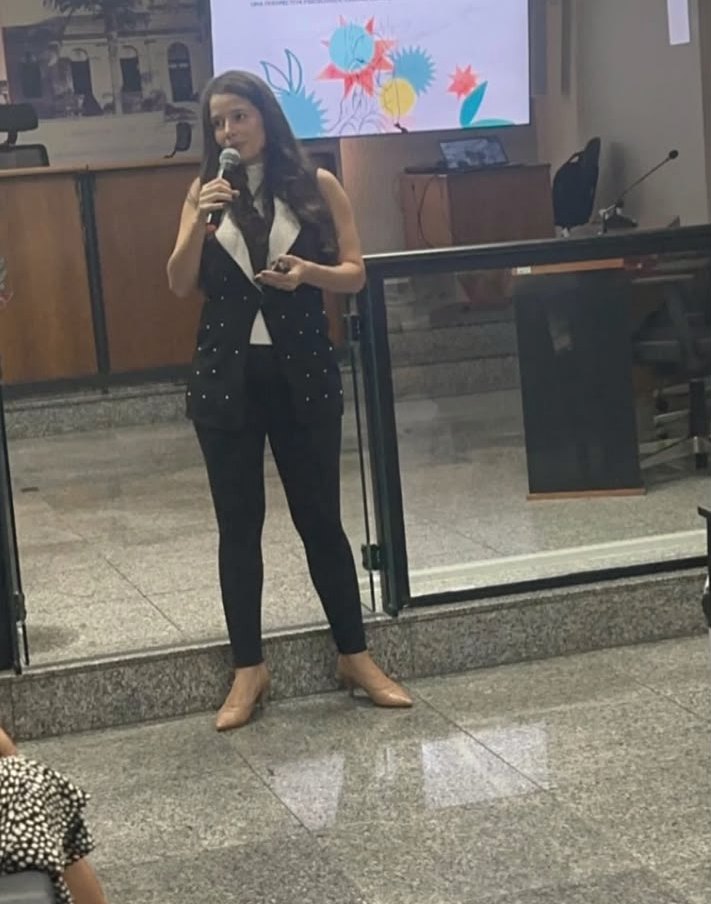 Aline Beringhs apresentando uma palestra, com slides projetados ao fundo